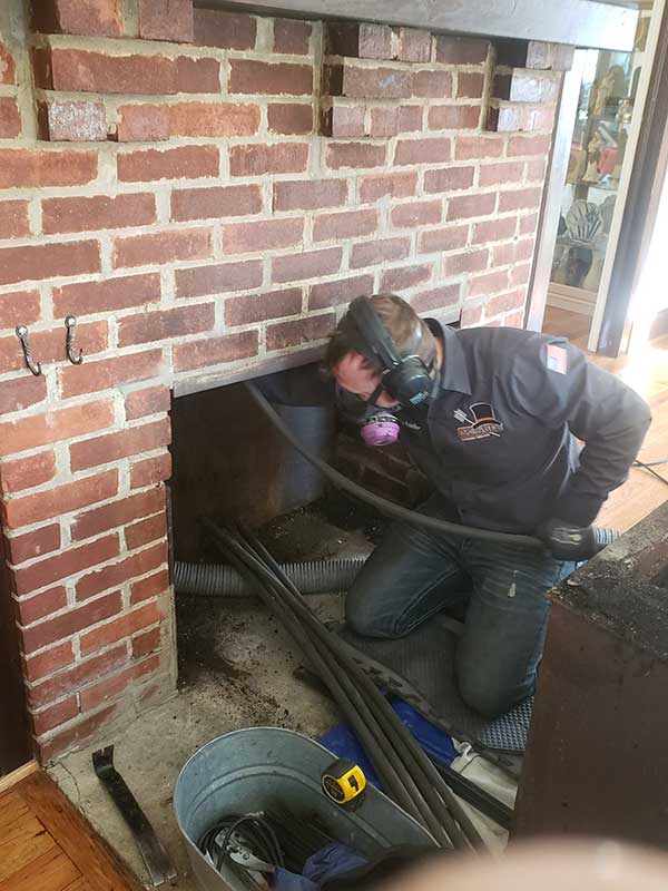 Chimney tech sweeping brick chimney with all his tools laid out and proper safety equipment